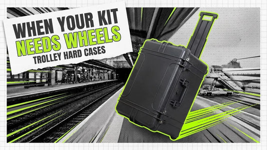Wheeled black hard case with extended handle rolling past a railway platform, label reading When Your Kit Needs Wheels
