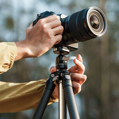Tripod in use with camera mounted and hands adjusting the head