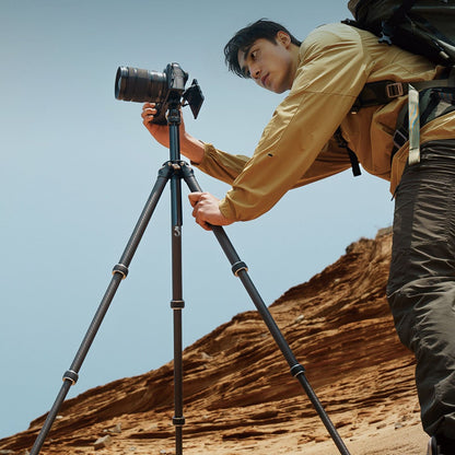Tripod set up on uneven ground with camera mounted and user adjusting