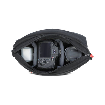 Open black sling bag interior with camera body, lens, and accessory pockets